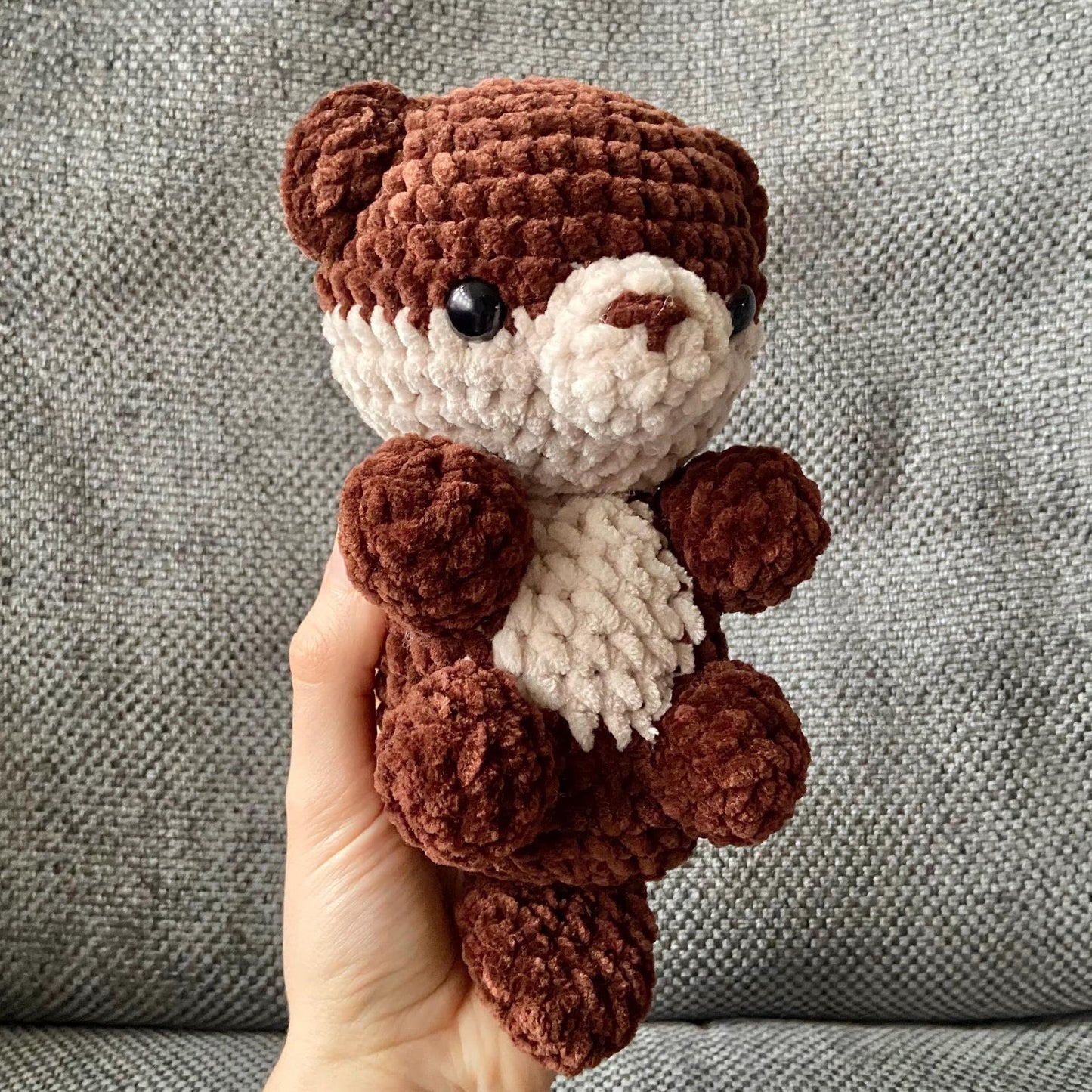 Finished crochet otter being held up behind a neutral background