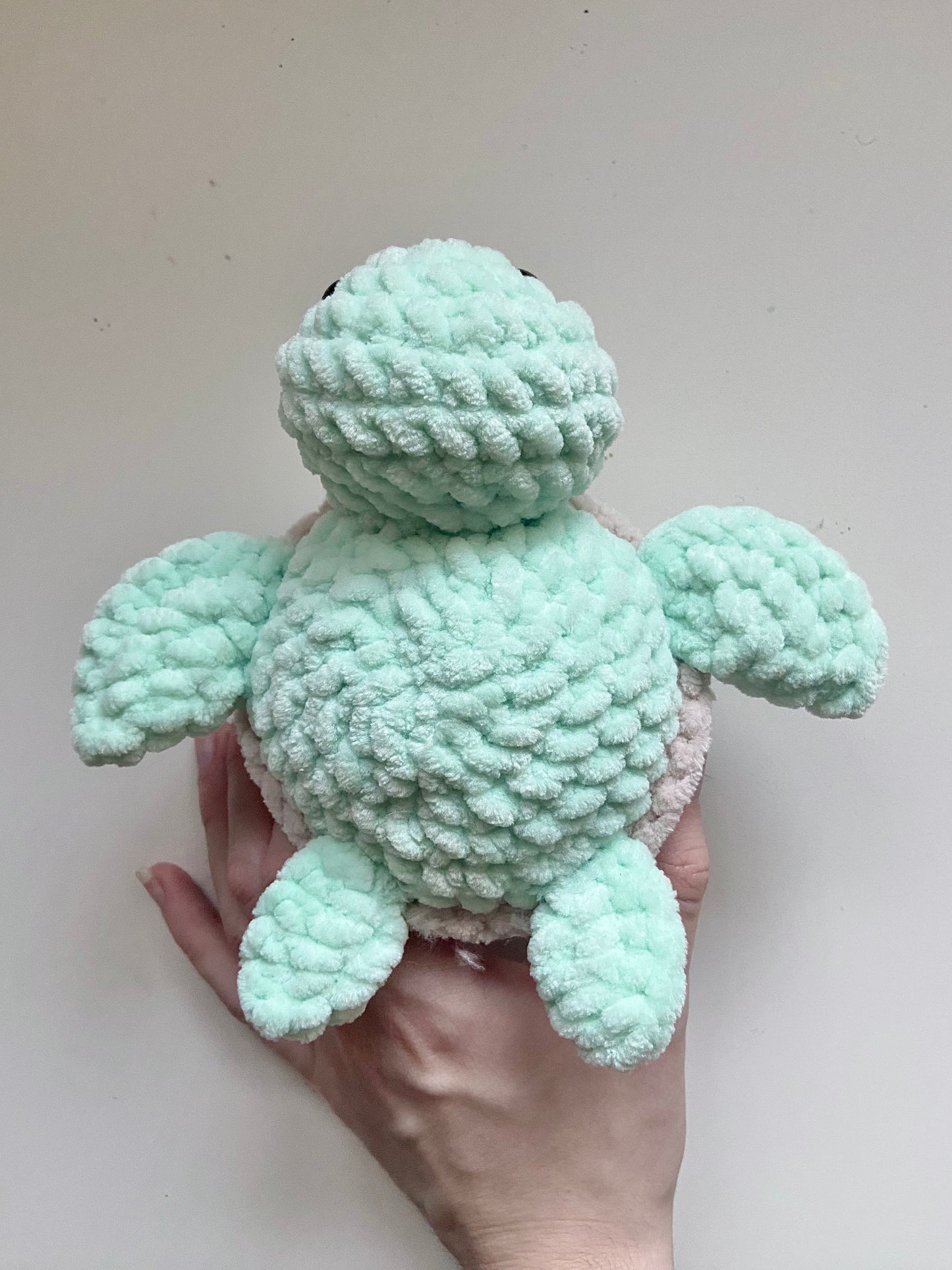 The bottom of a completed turtle toy being held up by a hand on a white background