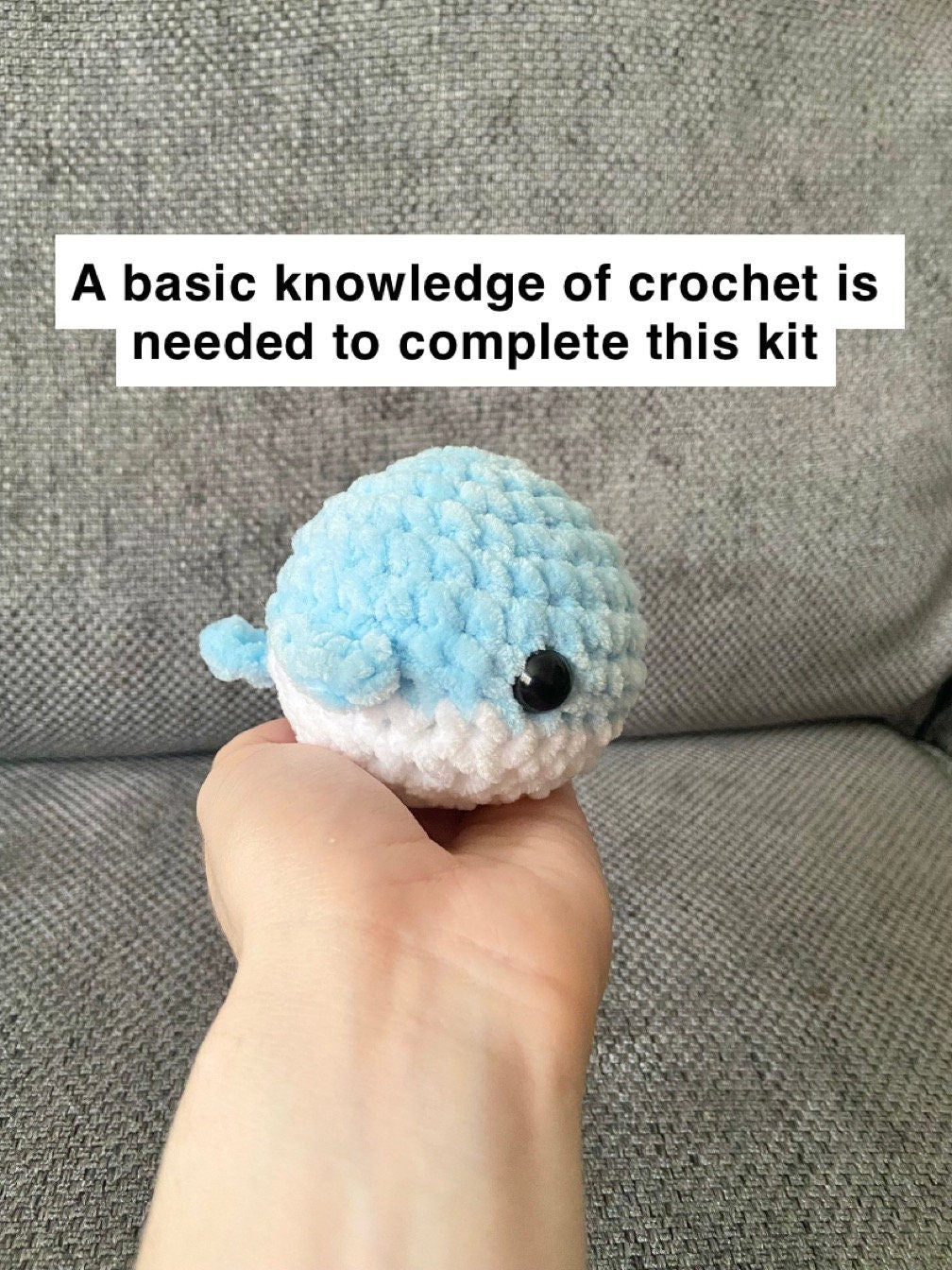 Completed crochet whale being held up behind a neutral background