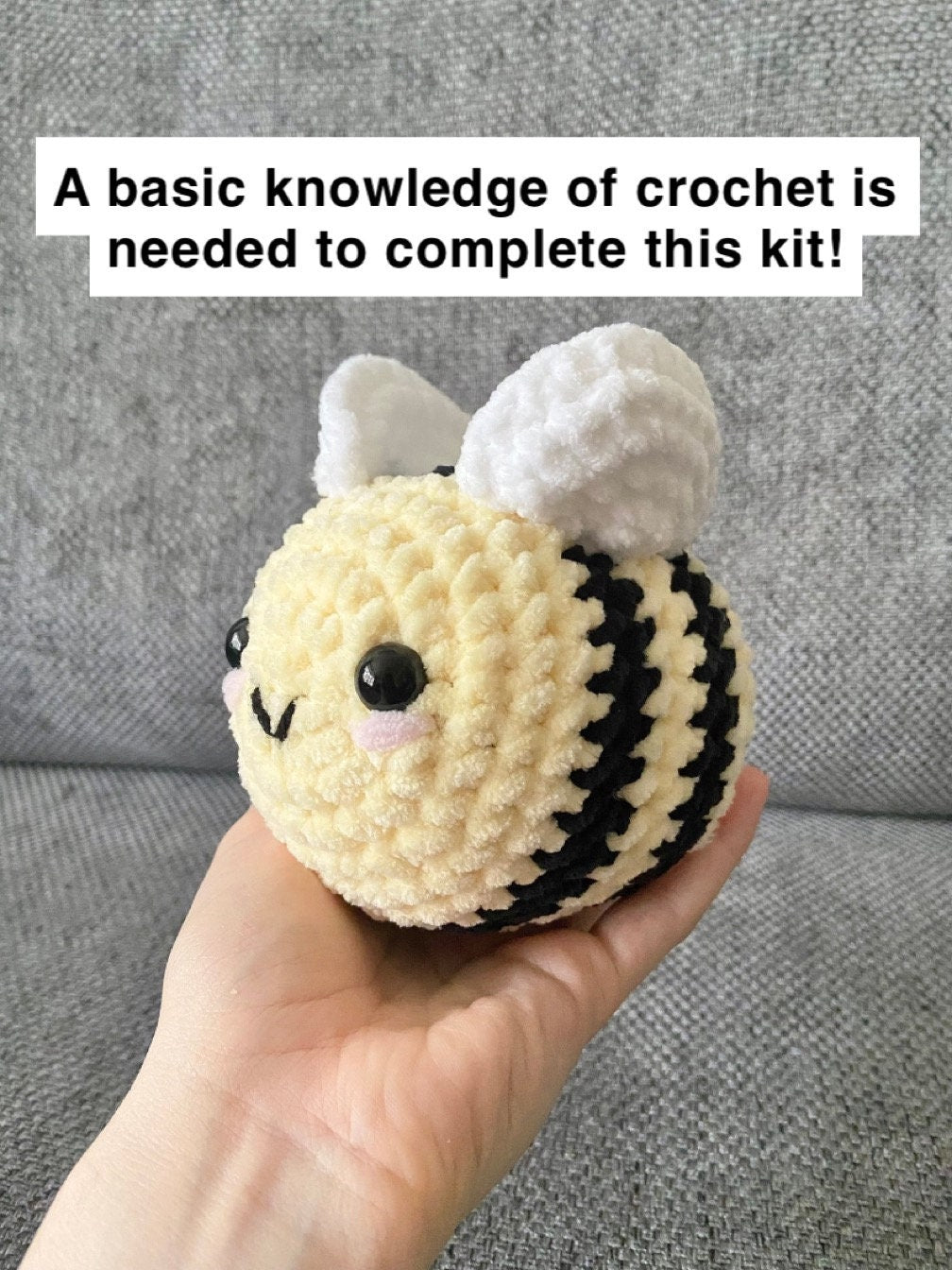 Finished crocheted bee being held up behind a neutral background