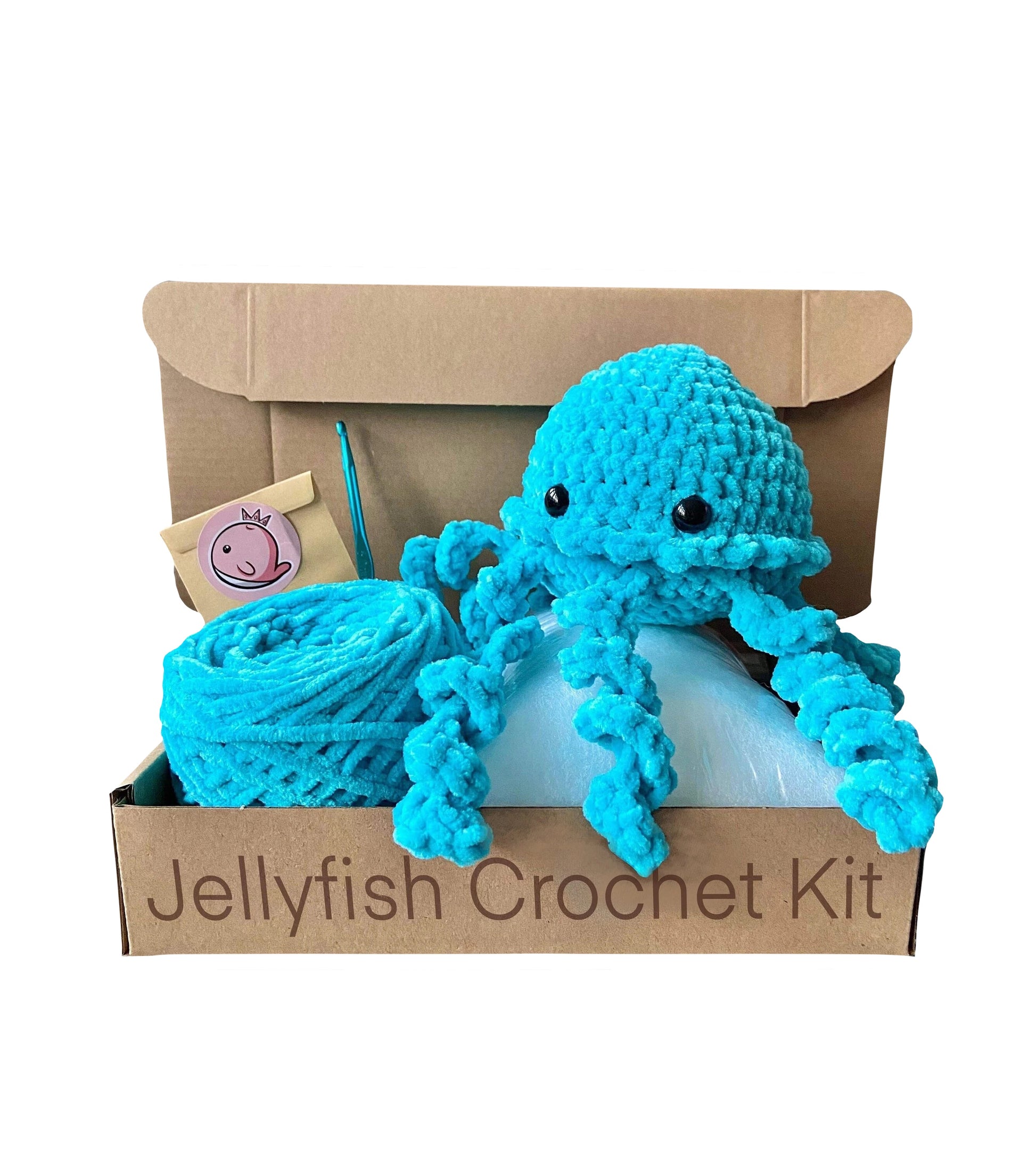 Crochet jellyfish on top of an open cardboard box including chenille yarn, crochet hook and a bag of toy stuffing