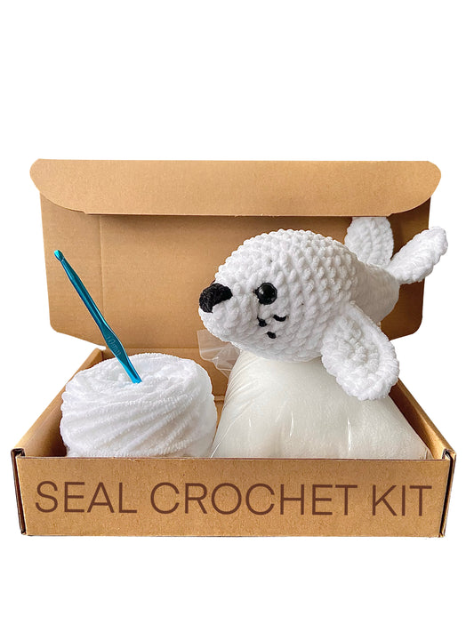 Handmade crochet seal on top of an open cardboard box including toy stuffing, white chenille yarn and a crochet hook