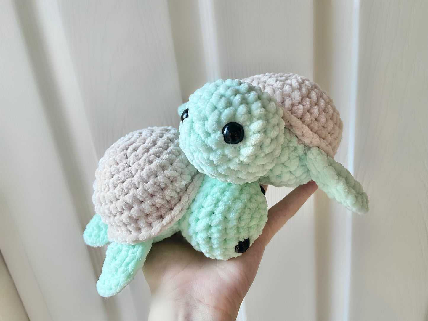 Two completed crocheted turtle plushies being held up by a hand
