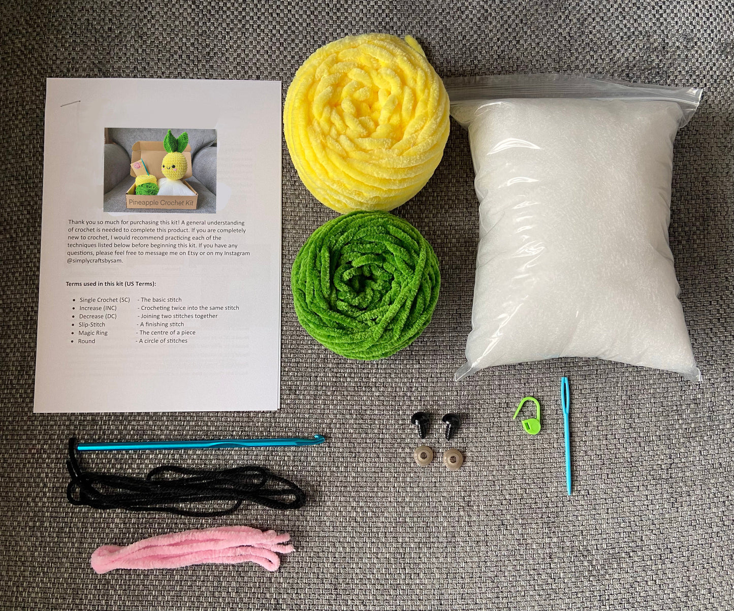 Contents of a pineapple crochet kit including two colours of chunky chenille yarn (yellow and green), a written Amigurumi crochet pattern, toy stuffing, crochet hook, embroidery thread, safety eyes and back, plastic needle and stitch marker 