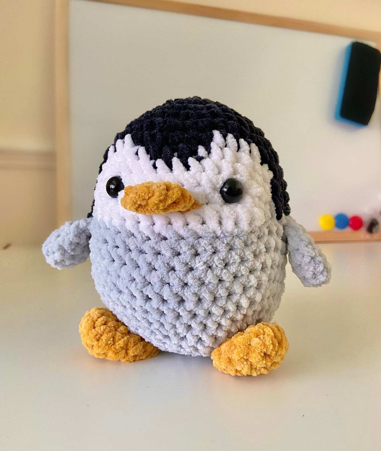 A finished crocheted penguin placed on a white desk