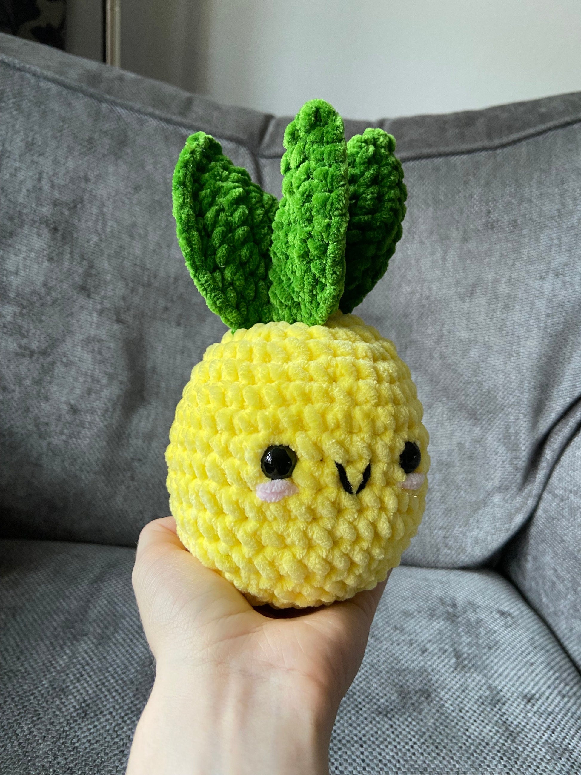 Finished crocheted Amigurumi pineapple being held up against a neutral background 
